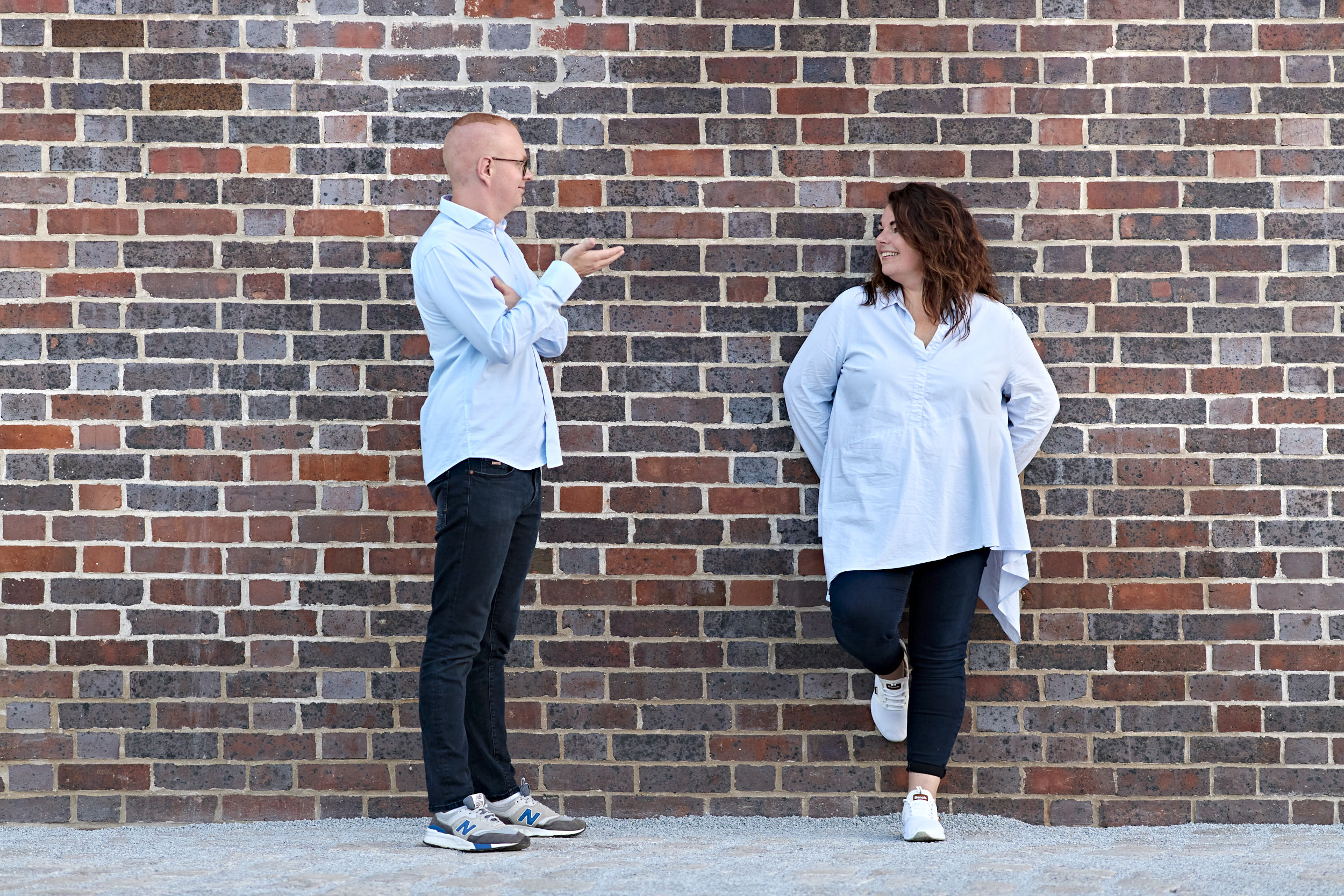 CVM_Antje_Arthur_Zusammenarbeit Arthur Fischer unterhält sich lächelnd mit Antje Schneider. Beide stehen vor einer Wand aus rötlichen Ziegeln.